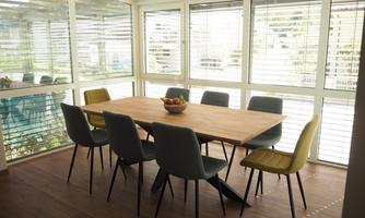 A bright dining room with a large wooden table and eight chairs. Large windows provide plenty of daylight and a pleasant atmosphere.