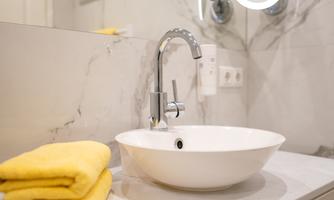 A modern bathroom with an elegant sink and a round mirror. Yellow towels are neatly placed on the shelf.
