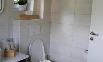A modern bathroom with a toilet and a small stool. There is a window on the wall and a plant.