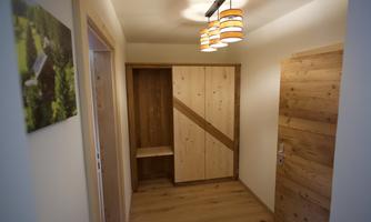 A bright hallway with wooden doors and a light wood wardrobe. The ceiling lamp has a modern design in orange and white.