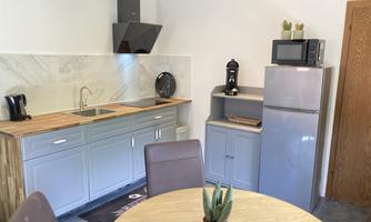 A modern kitchen with a wooden table and chairs. The kitchen unit includes a sink, stove, and refrigerator.