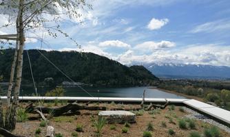 An idyllic landscape with a tranquil lake and a wooded hillside in the background. The sky is clear with a few clouds.