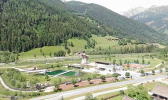 A picturesque landscape with green hills and mountains in the background. In the foreground, buildings and recreational facilities are visible.
