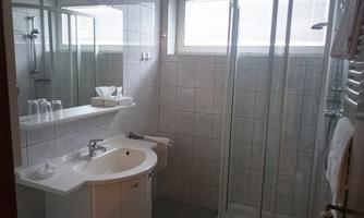A modern bathroom with a shower and a sink. It features bright tiles and large windows that provide good lighting.