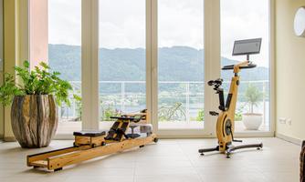A modern gym with a rowing machine and a stationary bike. Large windows offer a view of nature and plenty of daylight.