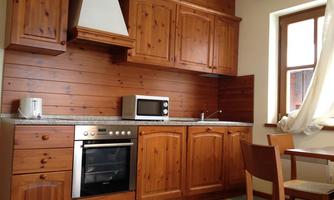 A modern kitchen with wooden furniture and a granite countertop. It is well equipped with a stove, a microwave, and a kettle.