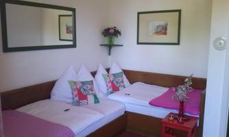 A cozy room with two beds and colorful cushions. Pictures hang on the wall, and a small table is in the center.