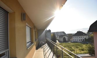 A sunny balcony overlooking houses and a green meadow. The sun is brightly shining in the sky.