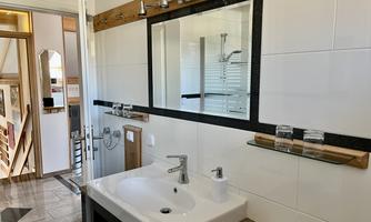 A modern bathroom with a large mirror and a sink. The walls are light tiled and there are wooden details for a cozy atmosphere.