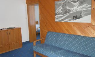 A cozy room with a blue couch and wooden walls. A picture of snow-covered mountains hangs on the wall.