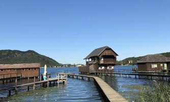 A picturesque lake with wooden piers and a beautiful house by the water. The surroundings are tranquil and surrounded by hills.