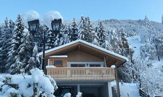 A cozy wooden house in the snow with a balcony.  
Surrounded by snow-covered trees and clear sky.