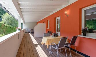 A beautiful outdoor area with wooden decks and orange walls. There is a table with chairs and plants for a cozy atmosphere.