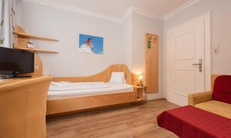 A cozy bedroom with a single bed and a red sofa. A picture with a winter sports motif hangs on the wall.