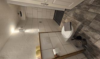 A modern bathroom with bright tiles and elegant wooden accents. It includes a toilet, a shower, and basic toiletries.