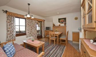 A cozy apartment with wooden furniture and a dining area. The windows are adorned with curtains, and the floor is covered with a carpet.