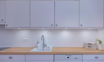 A modern kitchen with white upper cabinets and a bright wooden work surface. The sink area is designed to be simple and elegant.