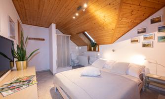 A cozy bedroom with a wooden ceiling and a large bed. On the wall, there are photos and a modern TV unit.