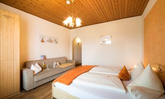 A cozy bedroom with a large bed and a sofa bed. The wooden floor and warm colors create an inviting atmosphere.