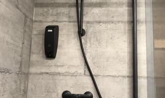 A black shower with a modern showerhead and a temperature control on a gray wall. The installation is minimalist and elegant.