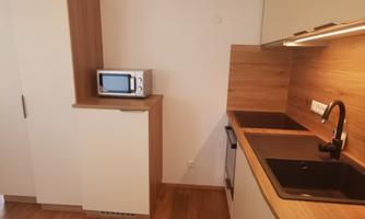 A modern kitchen with wooden and white elements. It features a microwave, a sink, and plenty of storage space.