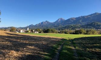 An idyllic landscape with mountains in the background and a clear blue sky. In the foreground, a field and a small village can be seen.