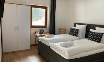 A cozy room with two beds, bright cushions, and a window. There is a table, a chair, and a wardrobe.