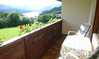 A quiet balcony overlooking a lake and green meadows. There are two chairs and a table to enjoy the view.