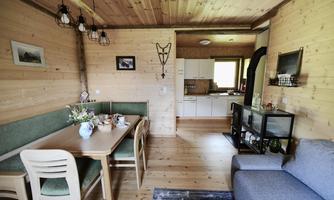 A cozy living space with wooden paneling, a dining table, and a kitchen in the background. A large sofa enhances the inviting atmosphere.