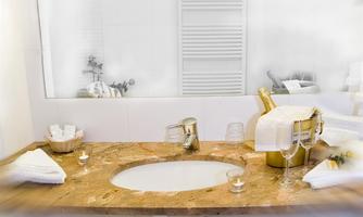An elegant bathroom featuring a round sink and a stylish marble table. In the background, glasses and a bottle of champagne create a relaxed atmosphere.