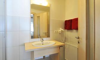 A modern bathroom with a shower and a sink. The walls are brightly tiled and there are towels in a vibrant red.