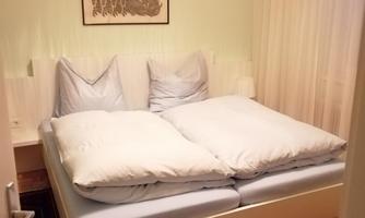 A cozy bedroom with a large bed and light bedcovers. A picture hangs on the wall, and the room has curtains and a carpet.