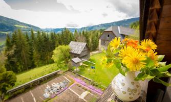 A beautiful view of a green landscape with mountains and trees. In the foreground, there is a vase with colorful flowers on a windowsill.