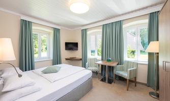 A modern hotel room with a comfortable bed and bright curtains. There is a table with chairs and a television on the wall.