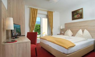 A cozy bedroom with a large bed and a television. The windows are bright and offer a view of the outdoors.