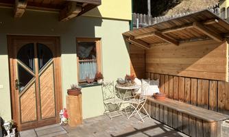 A cozy corner with a wooden bench and a table. The wall is painted green, and plants are decorated next to the door.
