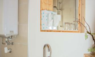 A modern bathroom with an elegant glass sink and a wooden-clad mirror. In the background, the wall tiles and a heating system are visible.