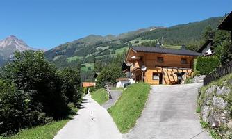 A picturesque mountain landscape with a wooden house and green meadows. In the background, a majestic mountain rises under a clear sky.