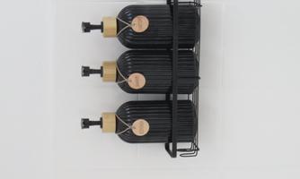 Three black bottles with wooden caps in a holder on a white wall. The bottles are labeled and have a modern and stylish appearance.