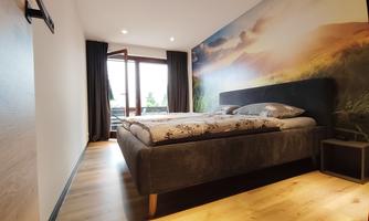 A modern bedroom with a large bed and a colorful wall design. Daylight streams in through the window, creating a pleasant atmosphere.