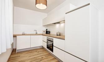 Modern kitchen with white furniture and wooden countertop. Bright and inviting space with a window and ceiling lamp.