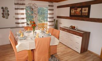 An elegant dining room with a large table set for a feast. The furniture is in warm colors, and large windows offer a view outside.