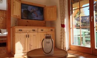 A cozy room with a wooden TV unit and a round table. Natural light comes in through the window, showing a view of the terrace.