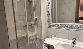 A modern bathroom with a shower and a sink. The walls are light tiled and there is a mirror with a decorative frame.