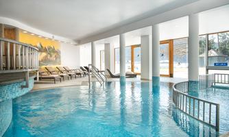 An elegant spa with an inviting pool and loungers. Large windows offer a view of the surrounding nature.