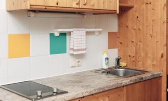 A modern kitchen with wooden cabinets and a covered countertop. Colorful tiles and a dish towel give the kitchen a fresh look.