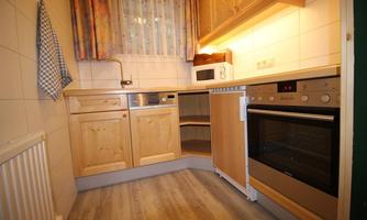 A cozy kitchen with wooden cabinets and modern appliances. The window with curtains provides bright light in the room.