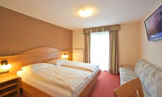 A cozy hotel room with a double bed and a seating area. The room has a warm color tone and a window with curtains.