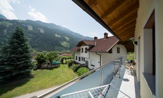 A beautiful balcony overlooking the mountains and a green meadow. The weather is sunny and clear.