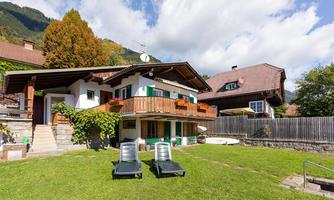 A typical alpine house with a balcony and blooming flowers. In the foreground, there are lounge chairs and a well-maintained garden.